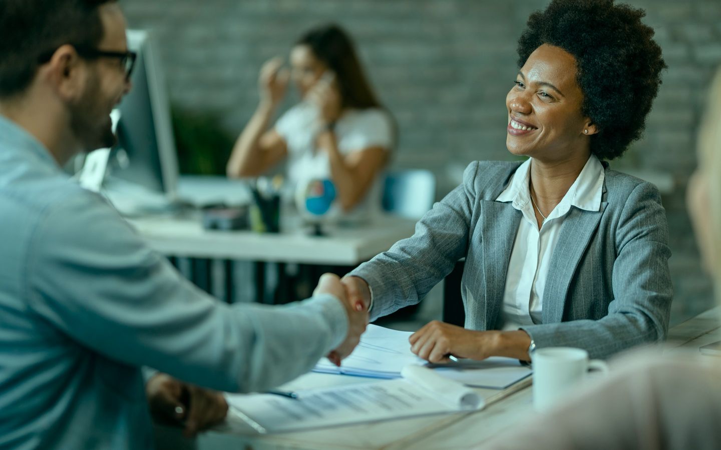 An HR manager smiling while shaking hands with a new colleague across a desk